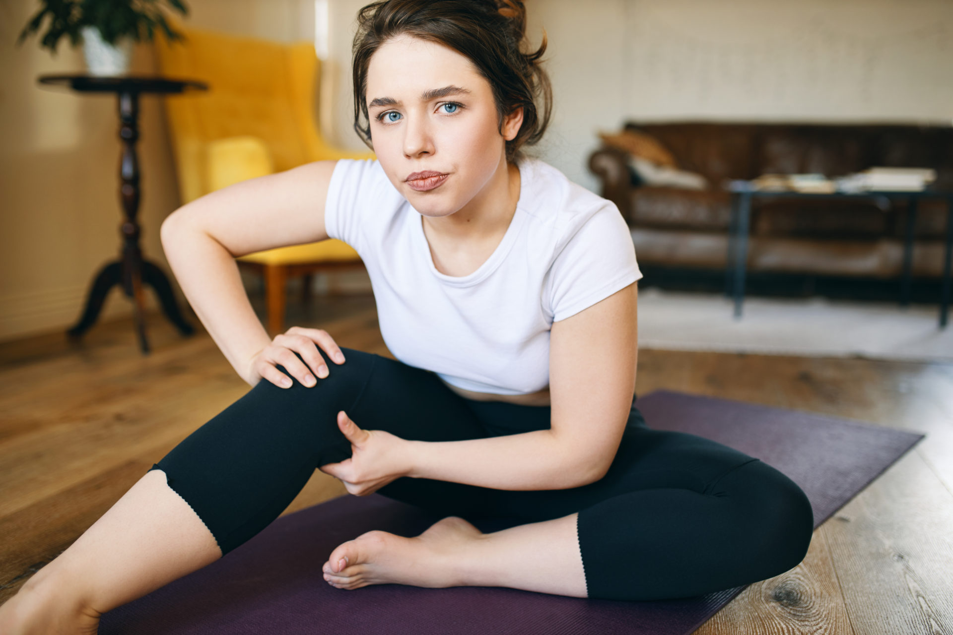 Upset frustrated young woman in sportswear feeling discomfort, tension and pain in her knee during yoga class because doing exercises incorrectly. Sports injury, trauma and fitness concept