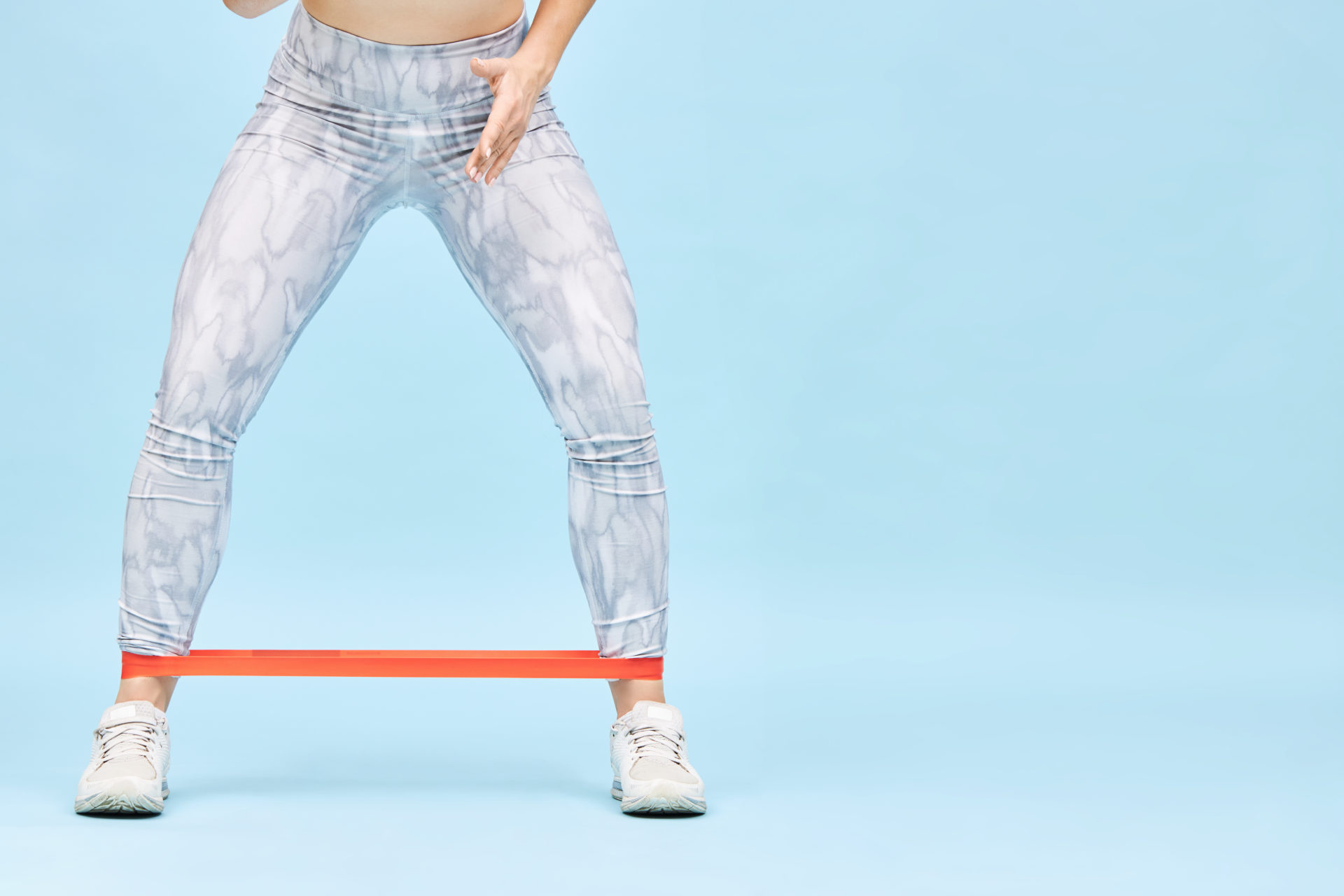 Strength, endrance and body shape. Cropped isolated image of woman in sportswear warming up training with resiatance band around her ankles, doing lateral walks, strengthening hip abductors leg strength woman